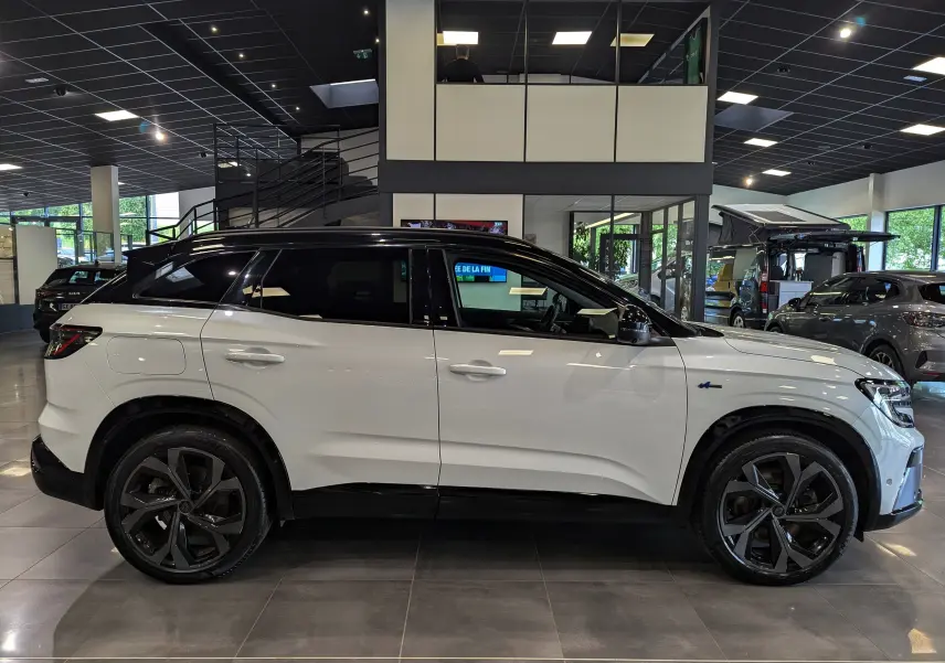 Vue latérale droite d'un Renault Austral blanc nacré avec toit noir et jantes noires en showroom.