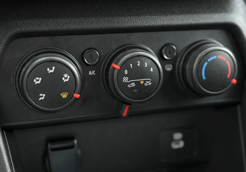 Gros plan sur les commandes de climatisation manuelle du Dacia Jogger 2024, boutons noirs avec indicateurs rouges et bleus.