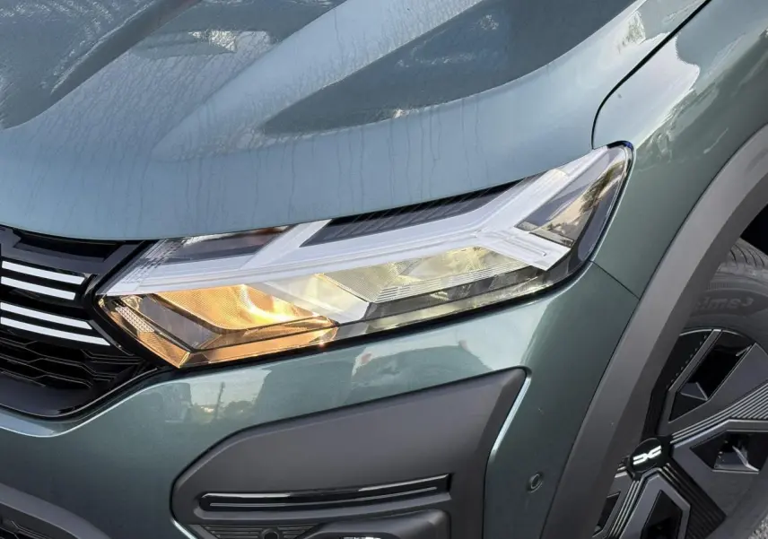 Gros plan sur le phare avant droit et la calandre du Dacia Jogger 2024 en Vert Cèdre avec jante noire distinctive.
