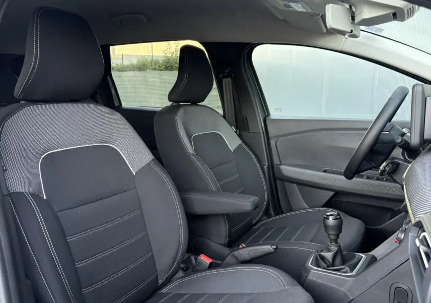 Vue intérieure côté conducteur du Dacia Jogger 2024, sièges tissu noirs avec surpiqûres blanches et boîte manuelle.