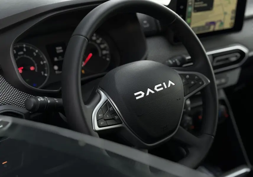 Vue rapprochée du volant noir de la Dacia Jogger 2024 avec commandes intégrées et écran GPS tactile visible en arrière-plan.