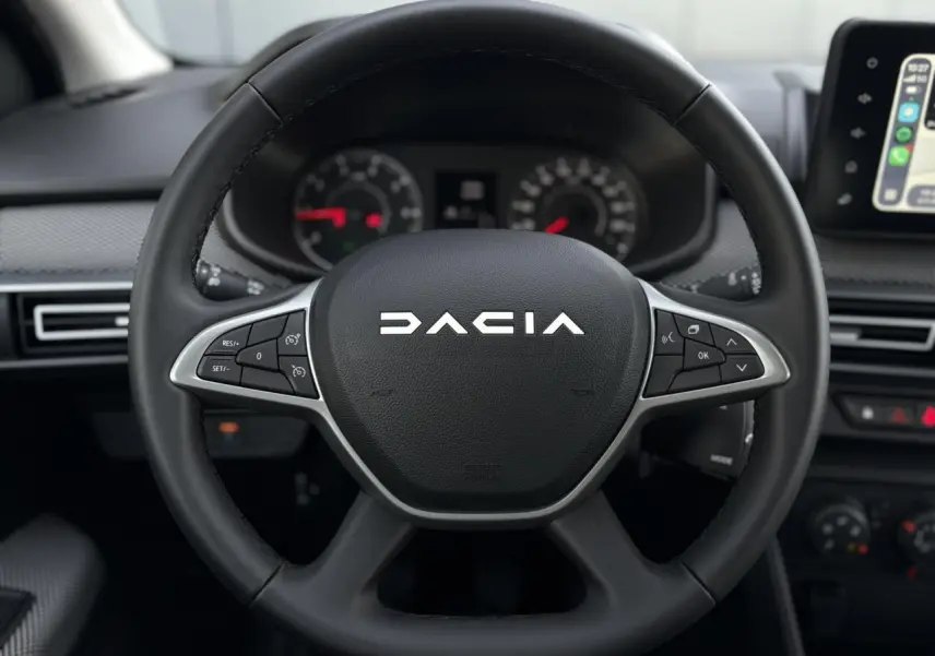 Vue rapprochée du volant noir de la Dacia Jogger 2024 avec commandes intégrées et tableau de bord en arrière-plan.