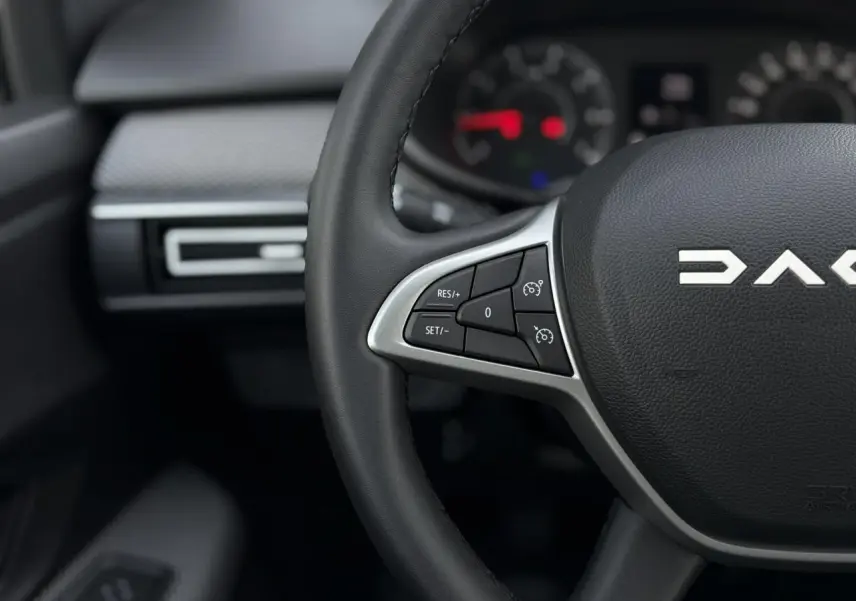 Gros plan sur le volant noir du Dacia Jogger 2024 avec commandes de régulateur de vitesse et tableau de bord flou.