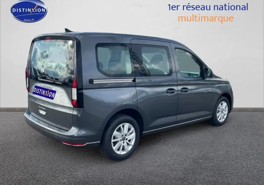 Vue 3/4 arrière droite d'un Volkswagen Caddy gris indien 2025 avec vitres teintées et barres de toit noires.