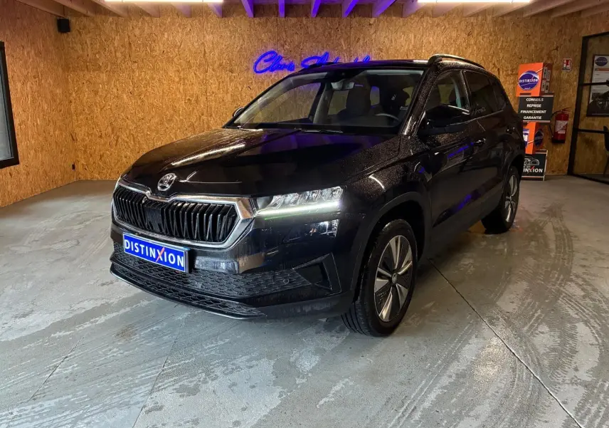 SKODA KAROQ noir 3/4 avant droit en intérieur, avec phares allumés et jantes alliage visibles.