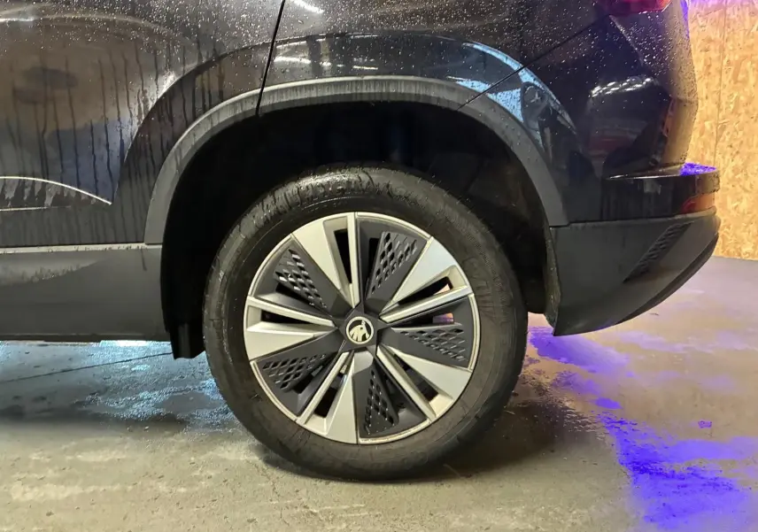 Vue latérale arrière droite du Skoda Karoq noir 2023, mettant en valeur la roue et la carrosserie mouillée.