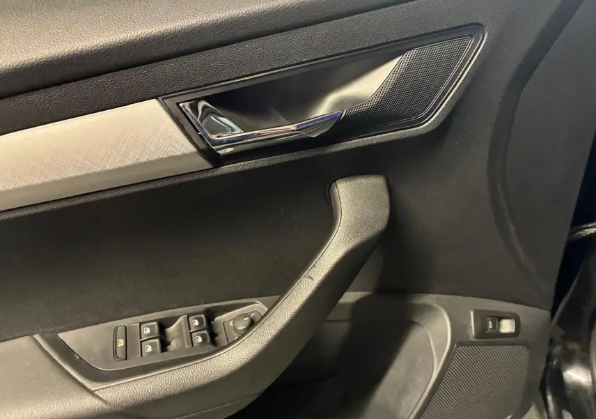 Détail de la porte avant gauche noire du Skoda Karoq 2023 avec commandes de vitres et poignée chromée.