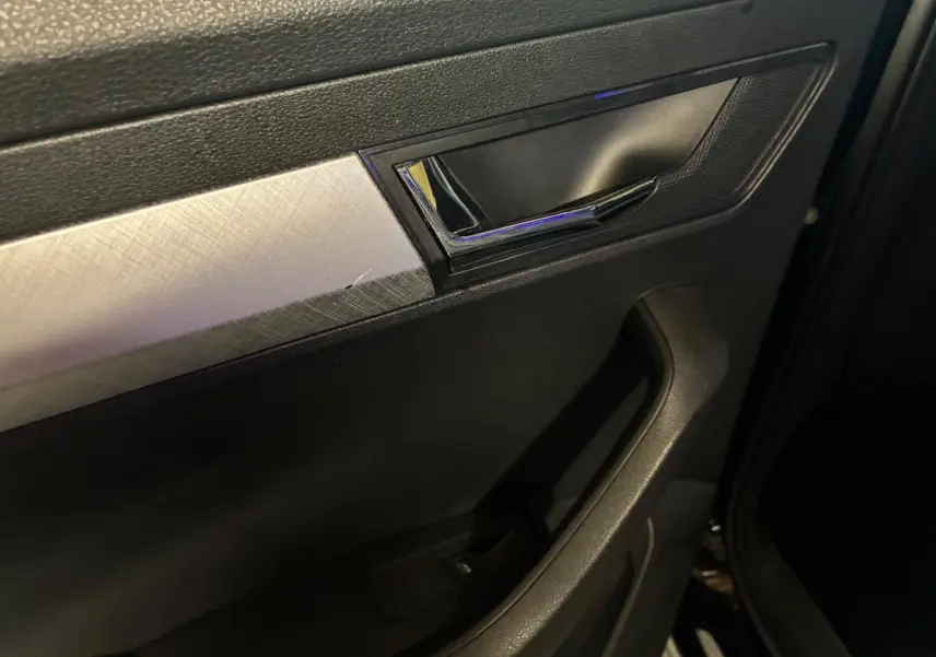 Détail de la poignée intérieure côté gauche d’une Skoda Karoq 2023 noire avec insert argenté texturé.