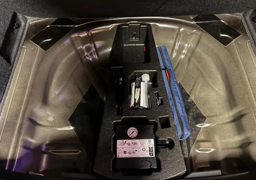 Vue plongeante sur le coffre ouvert d’un Skoda Karoq noir 2023, montrant le rangement sous plancher avec kit de réparation pneus.
