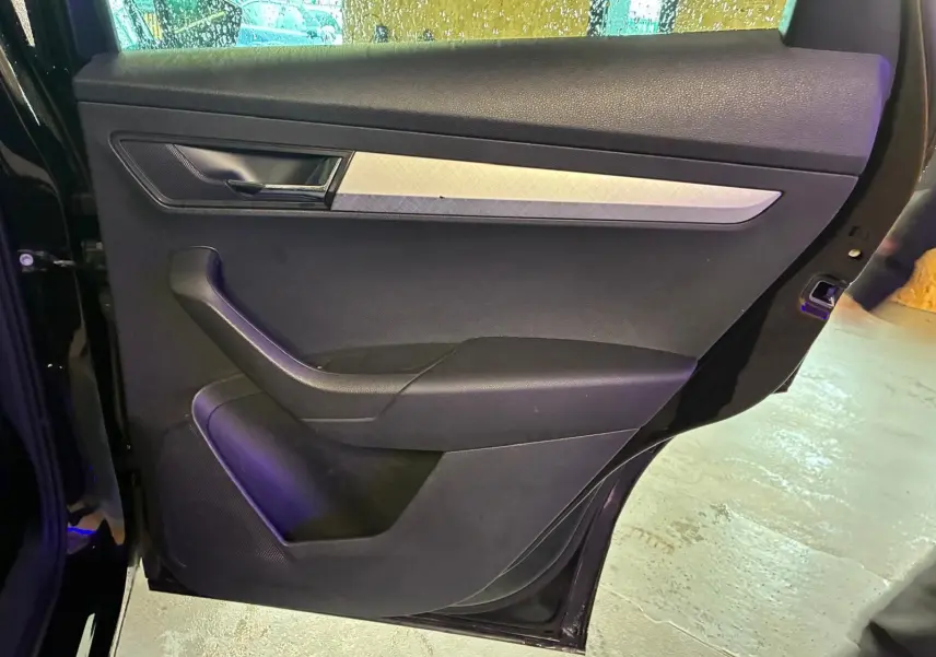 Vue intérieure de la porte arrière gauche noire du Skoda Karoq 2023, avec garniture tissu et insert décoratif argenté.