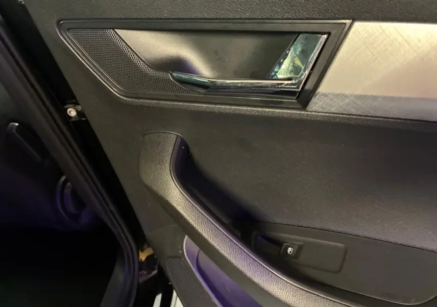 Gros plan sur la poignée intérieure et la commande de vitre côté gauche d'une Skoda Karoq noire 2023.