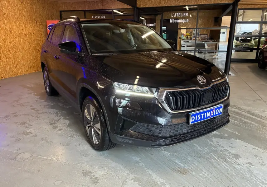 SKODA KAROQ noir 2023 vu en 3/4 avant droit dans un garage avec phares allumés et calandre distinctive.