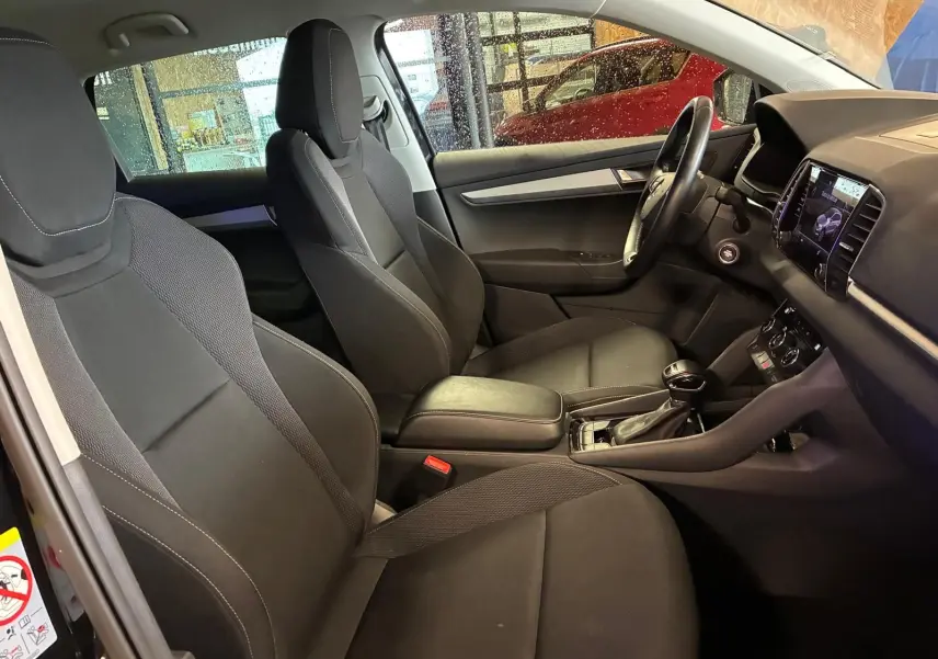 Vue intérieure côté conducteur du Skoda Karoq noir 2023, sièges tissu noir et tableau de bord avec écran tactile.
