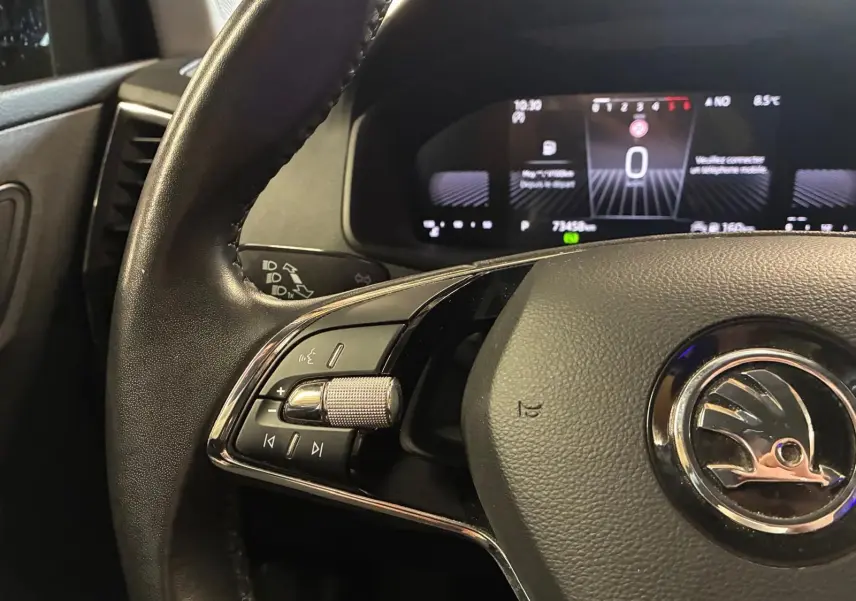 Gros plan sur le volant noir de la Skoda Karoq 2023 avec commandes intégrées et tableau de bord numérique en arrière-plan.
