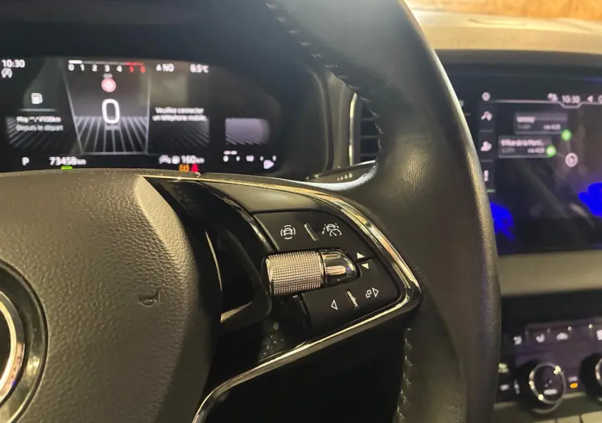 Gros plan sur le volant noir du Skoda Karoq 2023 avec commandes intégrées et tableau de bord numérique en arrière-plan.