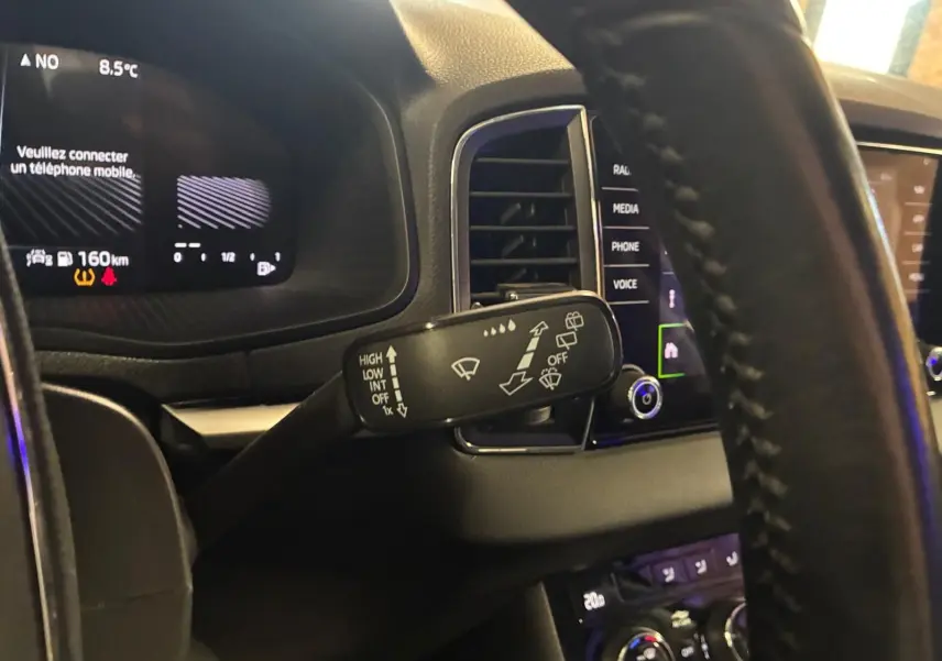 Vue intérieure rapprochée du volant et du commodo d’essuie-glace du Skoda Karoq noir 2023 avec tableau de bord digital.