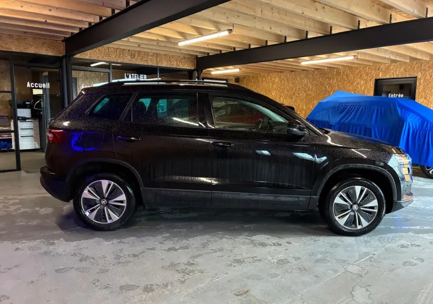 Vue de profil côté gauche d'un Skoda Karoq noir 2023 dans un garage avec toit en bois et sol béton.