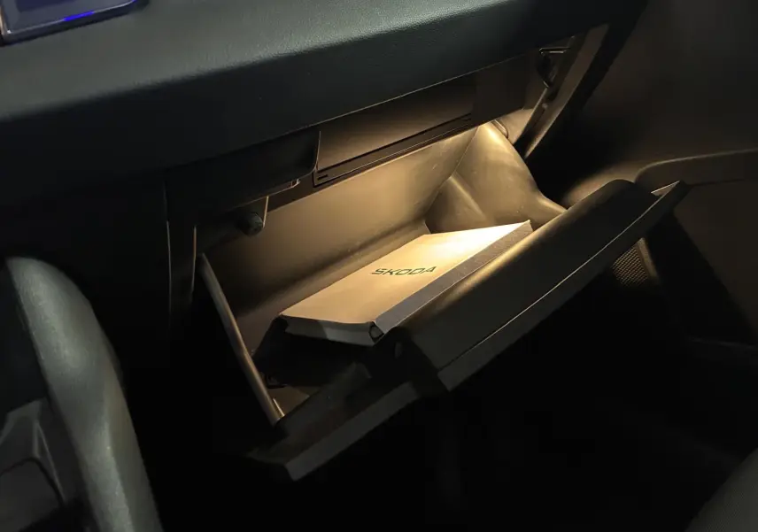 Vue intérieure en plongée sur la boîte à gants ouverte du Skoda Karoq noir, avec manuel éclairé à l'intérieur.