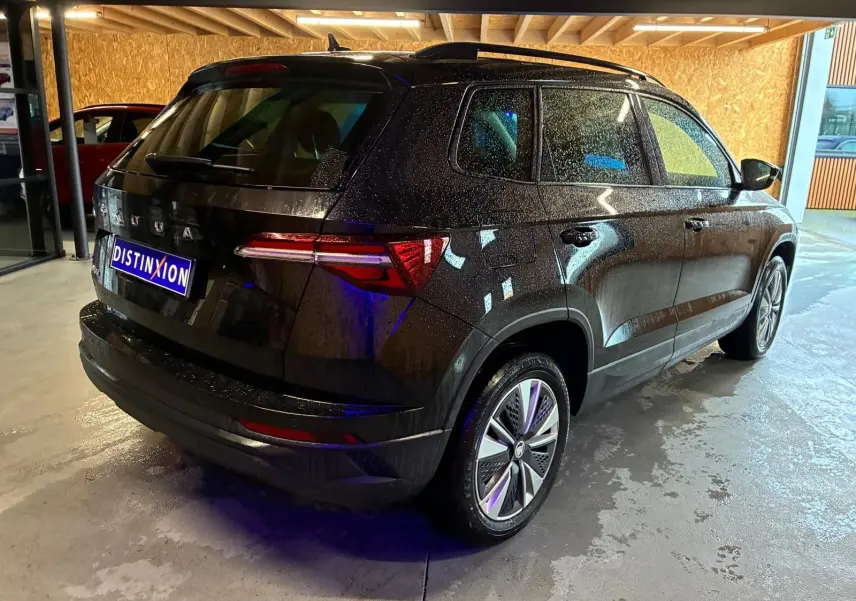 Vue 3/4 arrière droite d’un Skoda Karoq noir 2023 avec jantes alliage et feux arrière LED, stationné en intérieur.