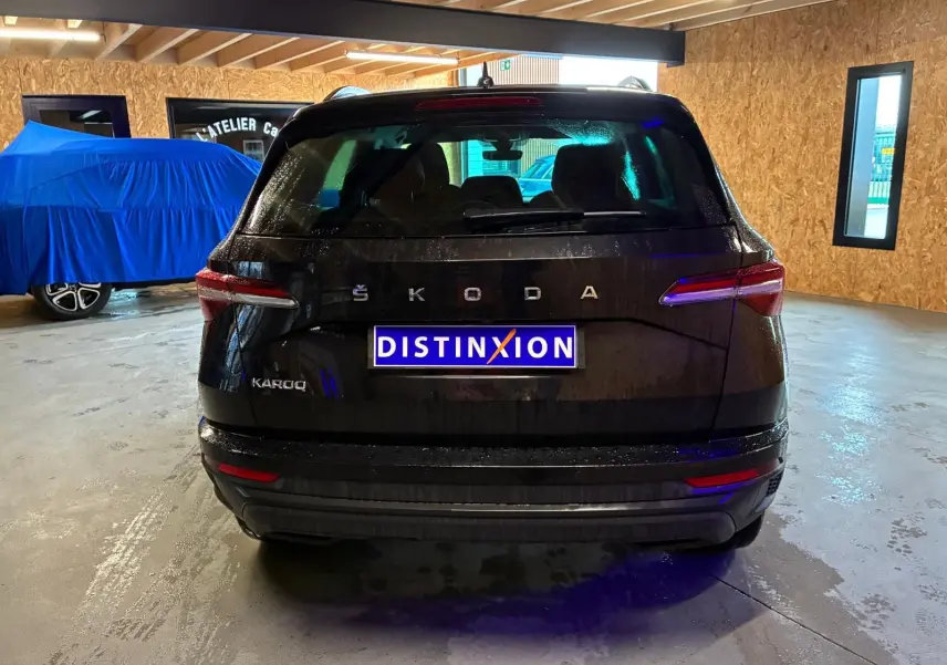 Vue arrière d'un Skoda Karoq noir 2023 dans un garage, avec logo ŠKODA et plaque Distinxion visible.