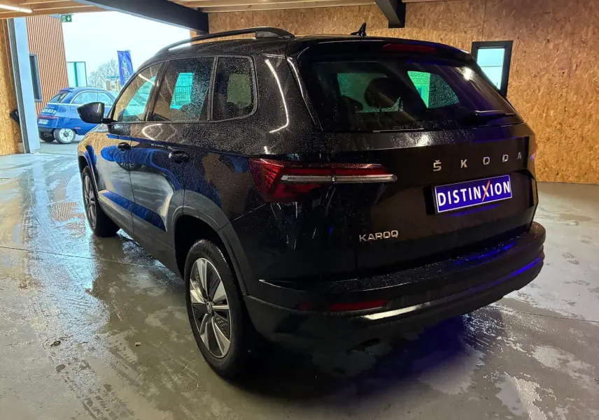 Vue 3/4 arrière droite d'un Skoda Karoq noir 2023 avec carrosserie brillante et feux arrière LED dans un garage.
