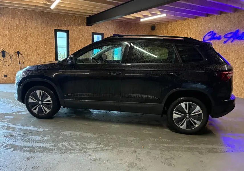 Vue de profil côté gauche d'un Skoda Karoq noir 2023 dans un garage avec murs en bois et sol béton humide.