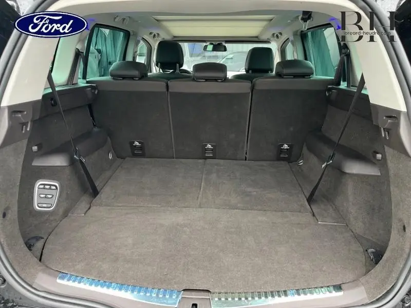 Coffre spacieux vu de l'arrière avec banquette noire en rang 3, intérieur sombre et toit panoramique visible.