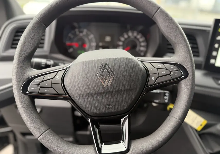 Gros plan sur le volant noir du Renault Master 2024 avec commandes intégrées et tableau de bord flou en arrière-plan.