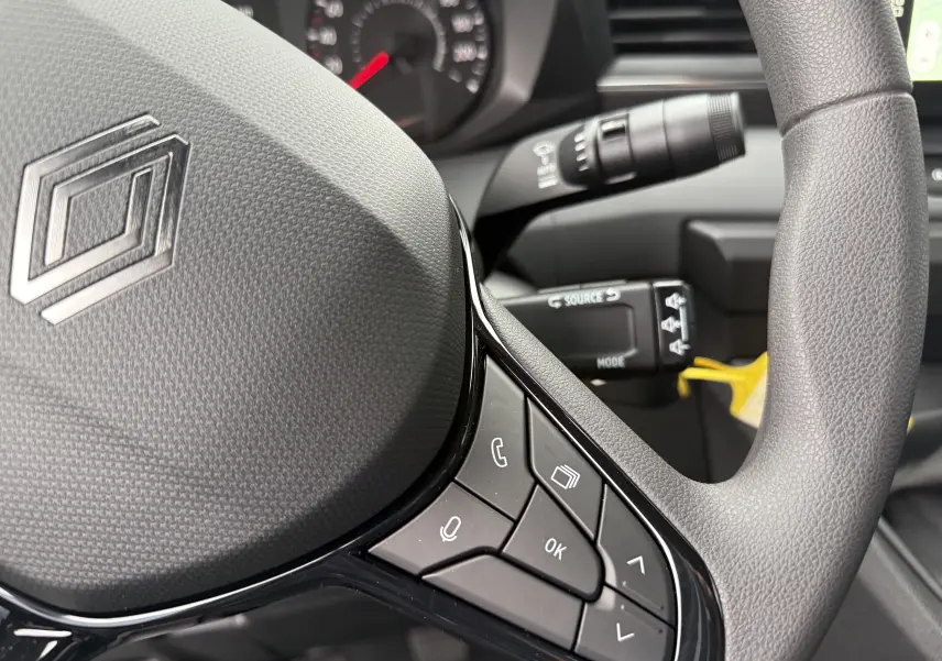 Gros plan sur le volant noir du Renault Master 2024 avec commandes intégrées et tableau de bord en arrière-plan flou.