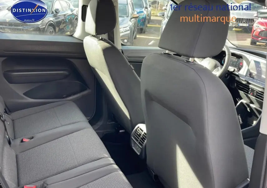 Vue intérieure arrière du Volkswagen Caddy 2.0 TDI 122 DSG7 2025 en tissu noir titane, montrant les sièges et la console centrale.