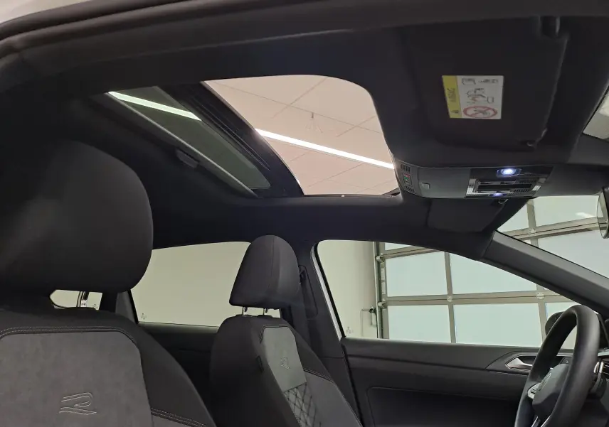 Vue intérieure avant du Volkswagen Taigo R-Line 2025 avec toit ouvrant en verre et sièges sport noirs avec logo R brodé.