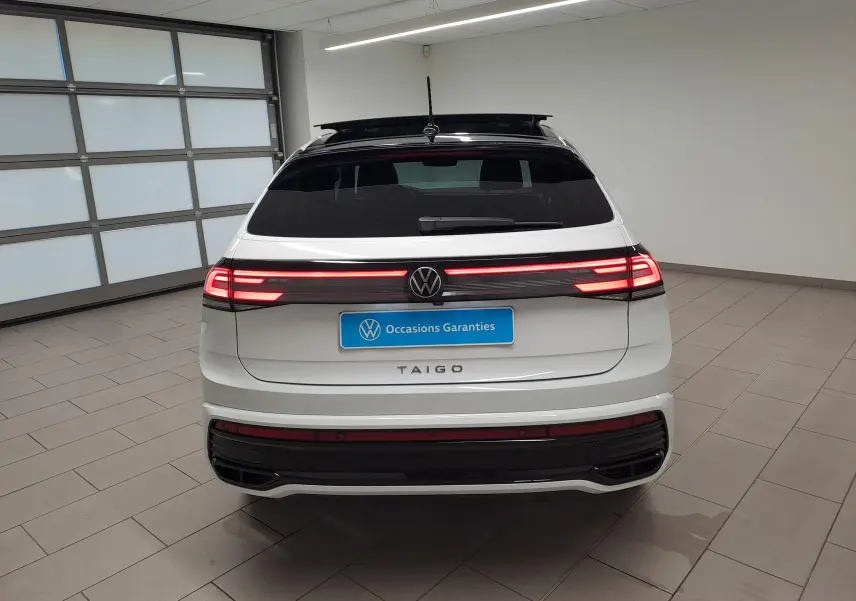 Vue arrière d'un Volkswagen Taigo blanc pur avec toit noir et feux arrière LED allumés dans un showroom.