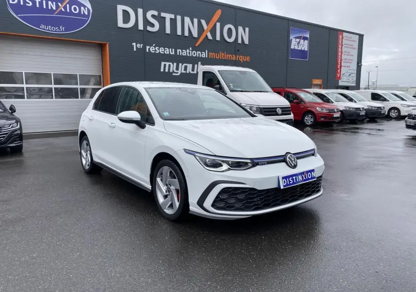 Volkswagen Golf 1.4 eHybrid blanche vue 3/4 avant avec calandre noire et jantes argentées sur parking humide