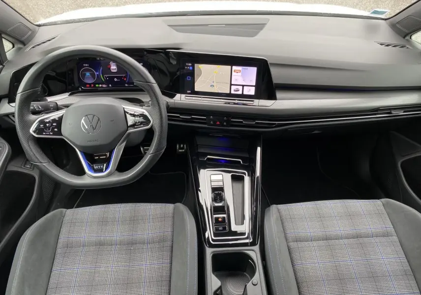 Vue intérieure avant de la Volkswagen Golf 1.4 eHybrid 2023, volant sport GTE et écran tactile central lumineux.