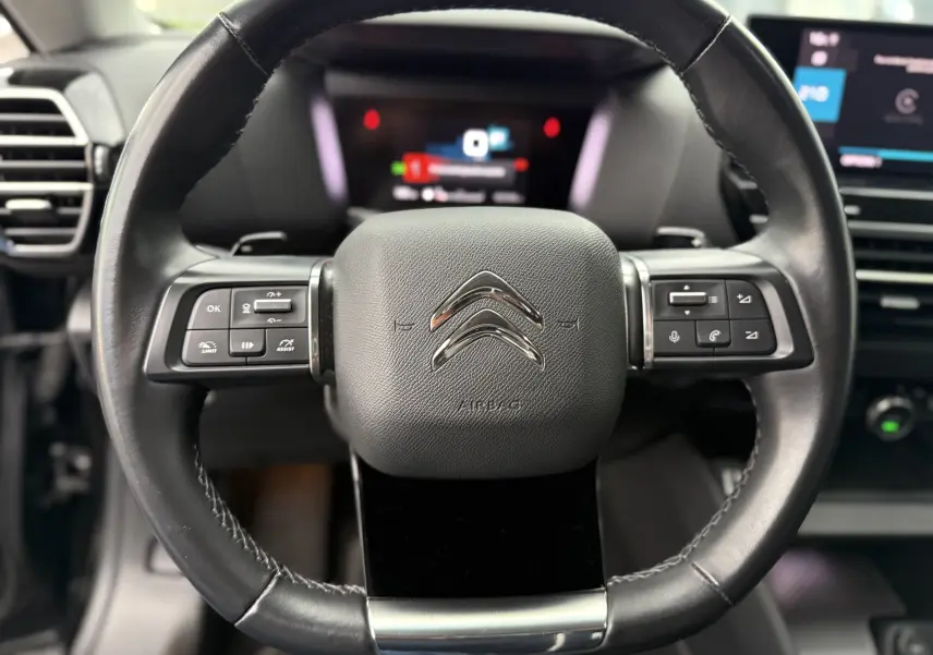 Gros plan sur le volant en cuir noir du Citroën C4 2022 avec commandes intégrées et logo chromé au centre.