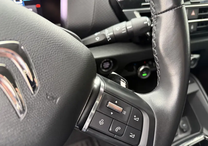 Gros plan sur le volant en cuir noir d'une Citroën C4 2022 avec commandes audio intégrées côté gauche.