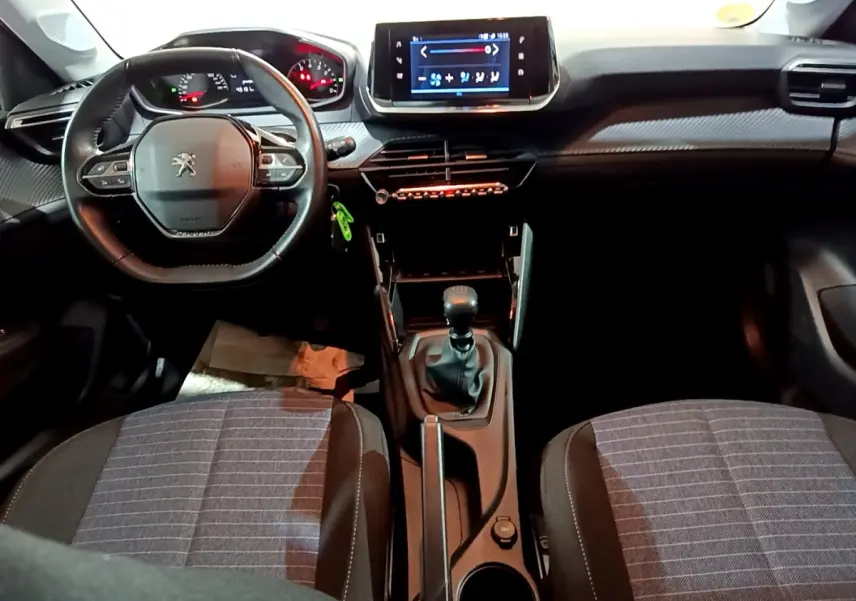 Vue intérieure avant de la Peugeot 208 1.5 BlueHDi 100 S&S Premium, montrant le volant compact, la console centrale avec boîte manuelle et l’écran tactile.