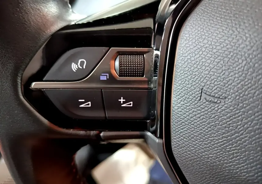 Gros plan sur les commandes vocales et volume au volant noir de la Peugeot 208 1.5 BlueHDi 2021.