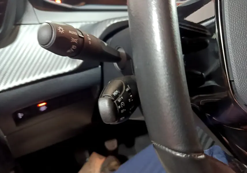Gros plan sur la colonne de direction et les commandes derrière le volant d'une Peugeot 208 blanche, intérieur noir.