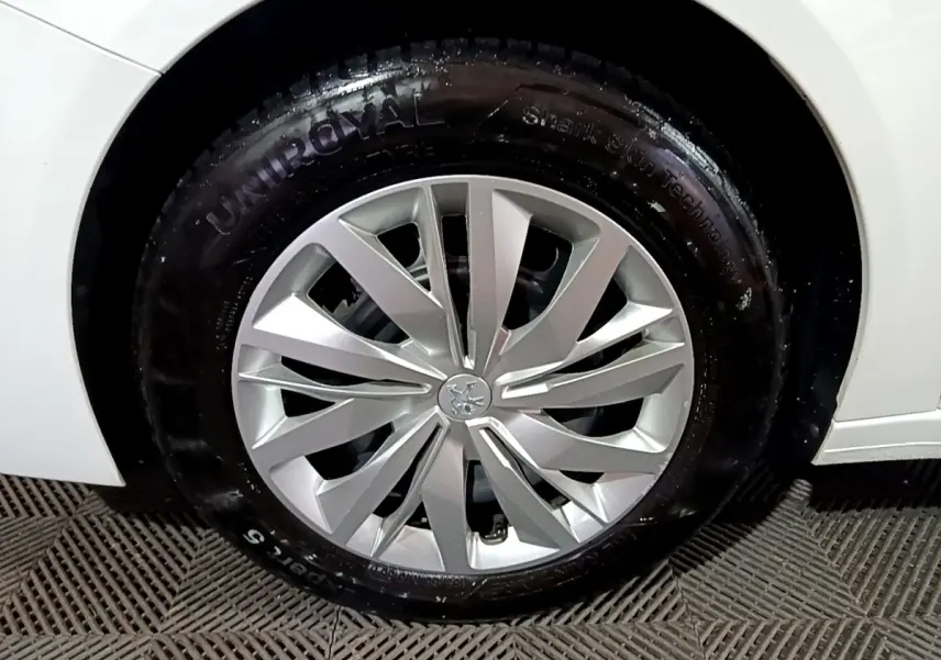 Gros plan sur la roue avant droite d'une Peugeot 208 blanche, mettant en valeur la jante argentée au design moderne.