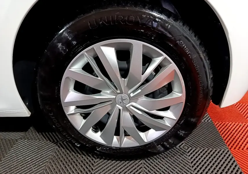 Gros plan sur la roue avant droite d'une Peugeot 208 blanche, mettant en valeur la jante argentée au design moderne.