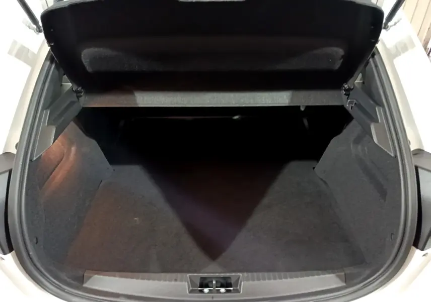 Vue plongeante sur le coffre ouvert d'une Peugeot 208 blanche, montrant l'espace de rangement vide et la doublure noire.