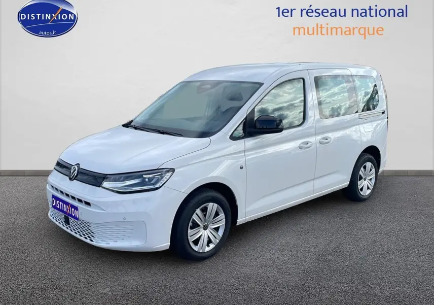 Volkswagen Caddy blanc vue 3/4 avant droit, avec barres de toit et vitres teintées arrière.