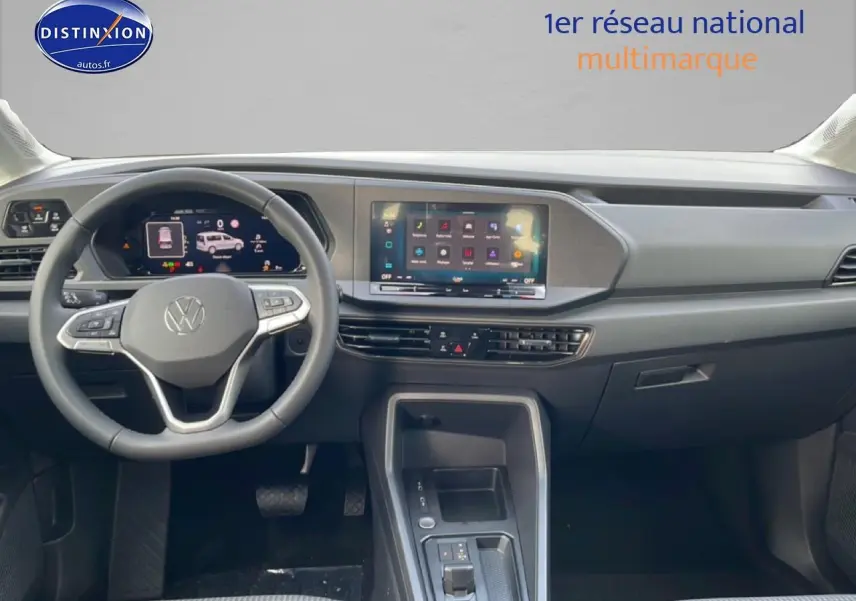 Vue intérieure frontale du tableau de bord du Volkswagen Caddy blanc 2025 avec écran tactile et volant multifonction cuir.