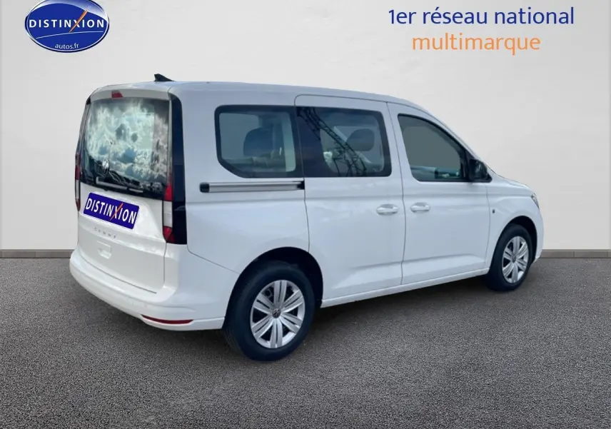 Volkswagen Caddy blanc vu en 3/4 arrière droit, avec vitres teintées et barres de toit noires.