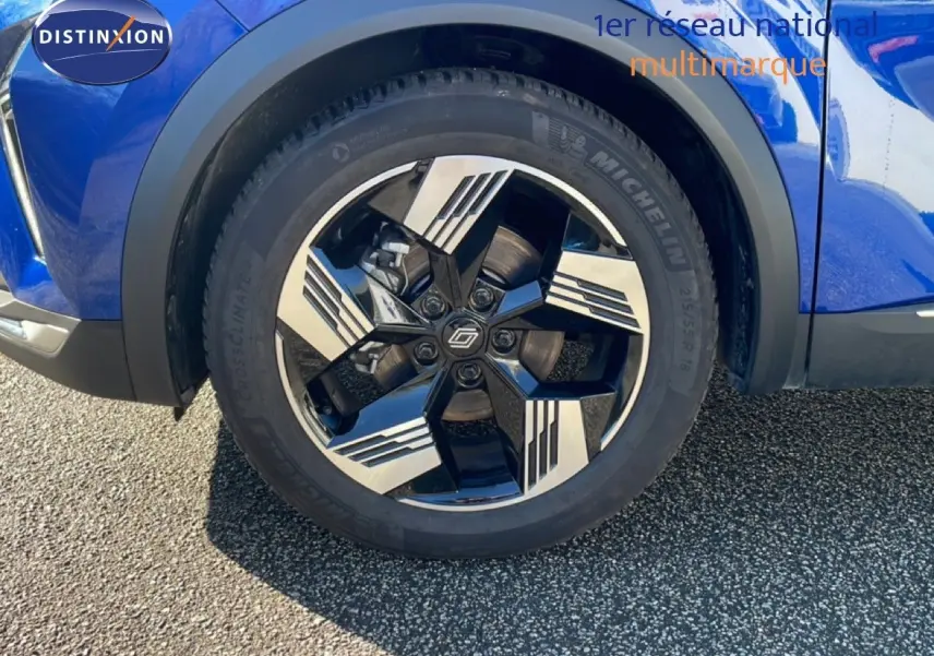 Gros plan sur la roue avant droite d’un Renault Symbioz bleu iron metal avec jante noire et argentée au design géométrique.