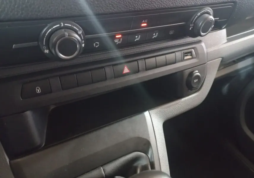 Gros plan sur la console centrale du Peugeot Traveller gris clair, avec commandes climatisation et port USB visible.