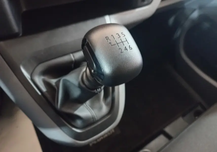 Gros plan sur le levier de vitesses manuel noir du Peugeot Traveller 1.5 BlueHDi 120, intérieur sombre.