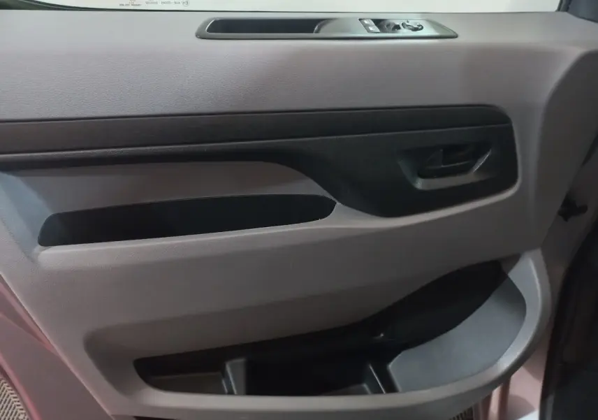 Détail de la porte intérieure côté conducteur du Peugeot Traveller gris clair, avec commandes des vitres et poignée noire.