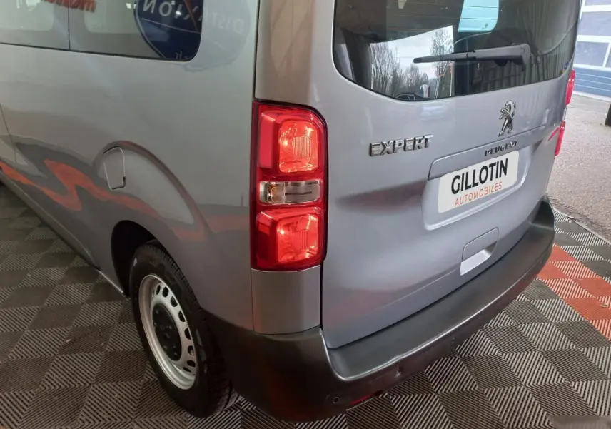 Vue 3/4 arrière droite d'un Peugeot Traveller gris clair avec feux arrière et logo Expert visibles.